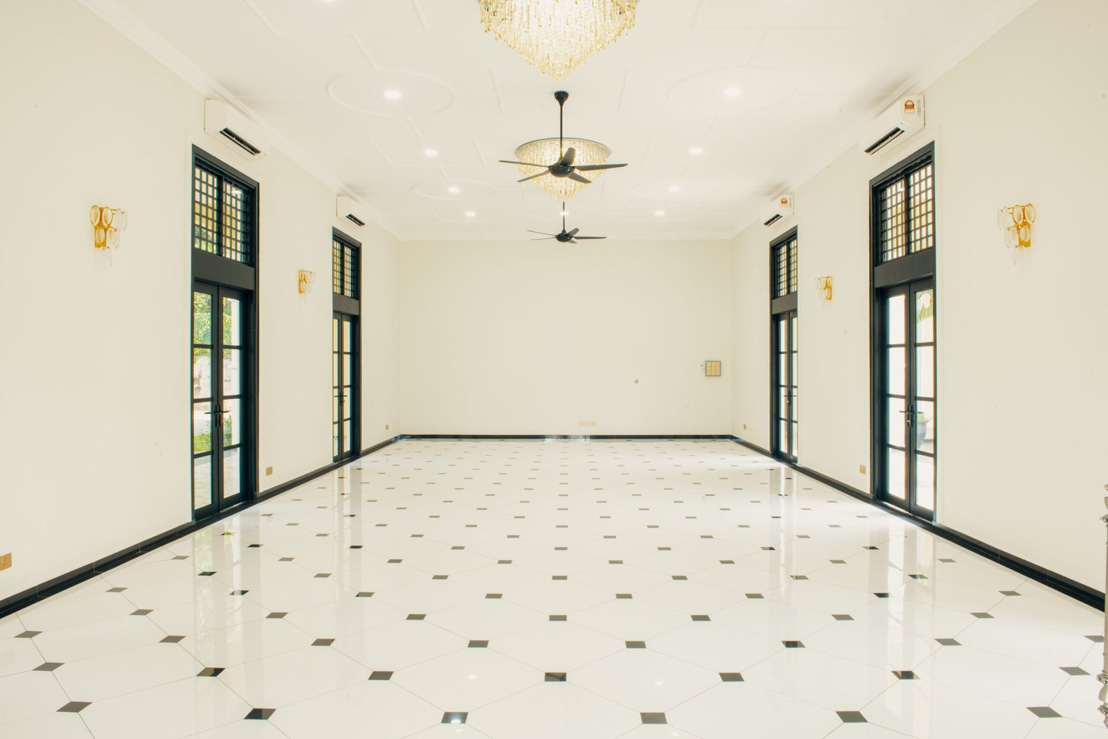 Spacious and elegant Grand Hall at The Agam, featuring chandeliers, large windows, and modern lighting for weddings and events.