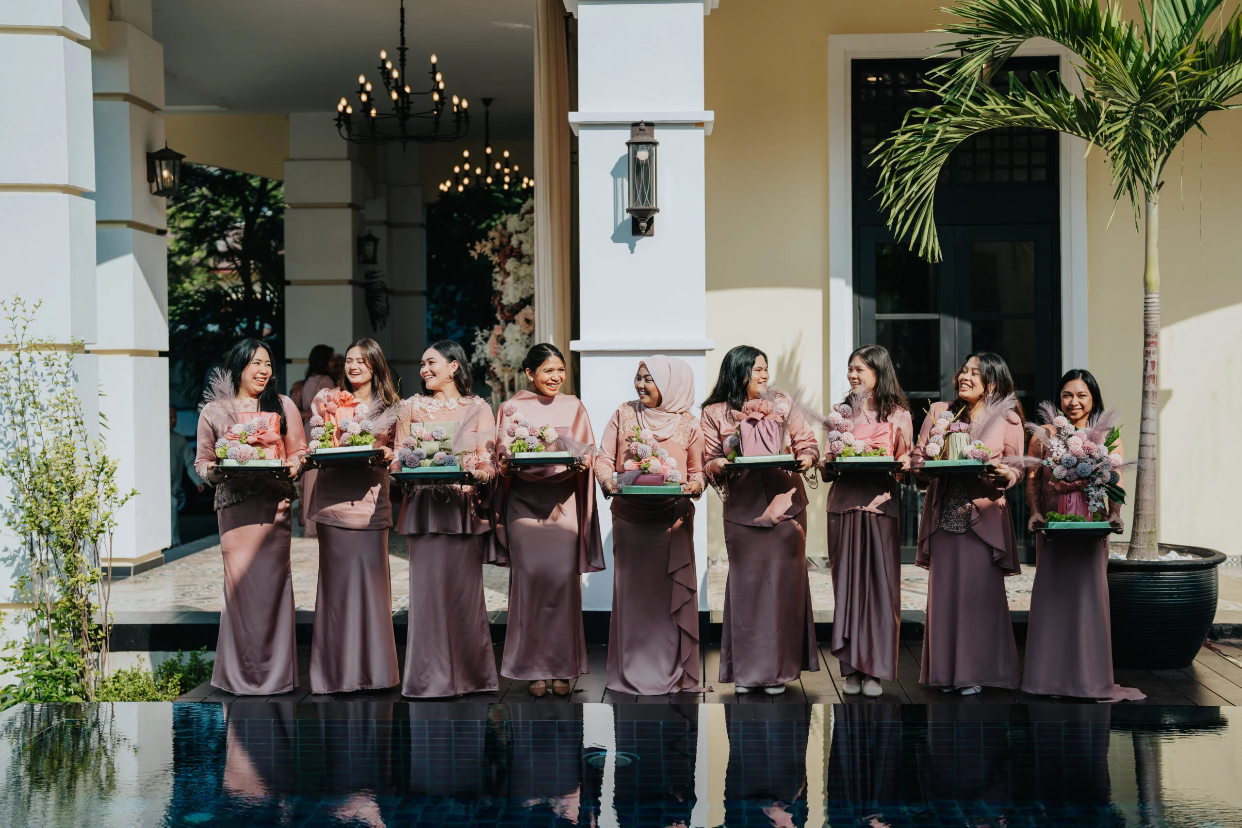 Bridesmaids in matching outfits holding floral arrangements, standing by the pool at The Agam, showcasing the venue’s wedding event services.