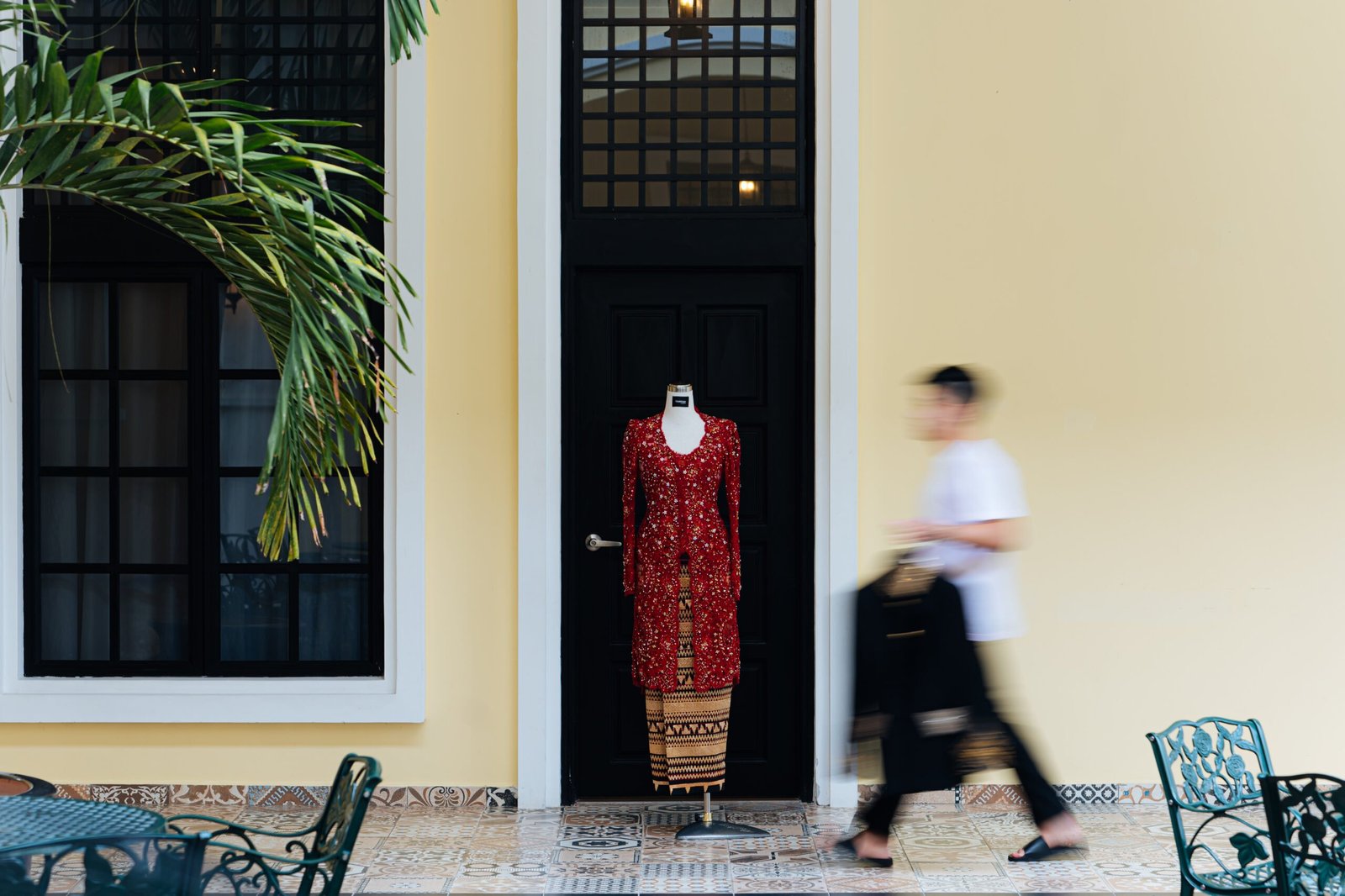 A traditional outfit on display at The Agam with a blurred figure walking past, representing the venue's cultural and event services.