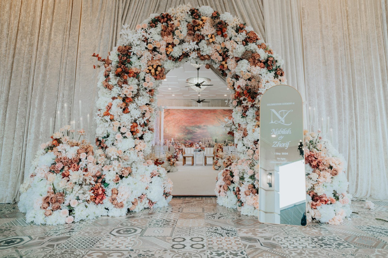 Beautiful floral wedding arch with pastel and autumn hues at The Agam, leading to an elegant wedding reception setup.