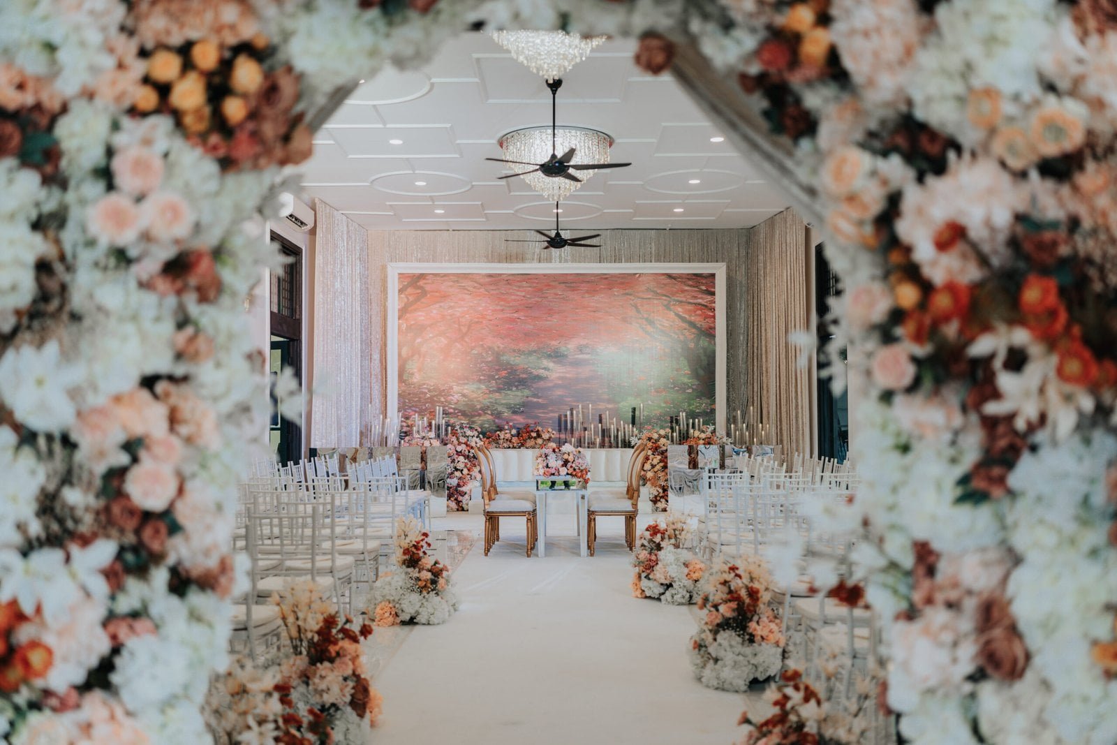 Romantic wedding aisle adorned with floral arrangements leading to an intimate ceremonial setup at The Agam, framed by an arch of blush and soft pink flowers.